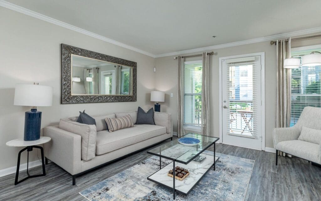 Two BR Apartments in Sandy Springs, GA - The Stratford - Living Room with Wood-Style Flooring, Rug, Glass Coffee Table, White Sofa, Armchair, Framed Mirror, and Side Tables