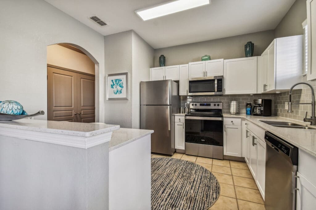 Studio Apartments In Tampa, FL - Seasons At Westchase - Oversized Gourmet Kitchen With White Quartz Countertops, White Cabinets, Breakfast, Bar, Tile Flooring, Double-Bowl Kitchen Sink, And Dishwasher