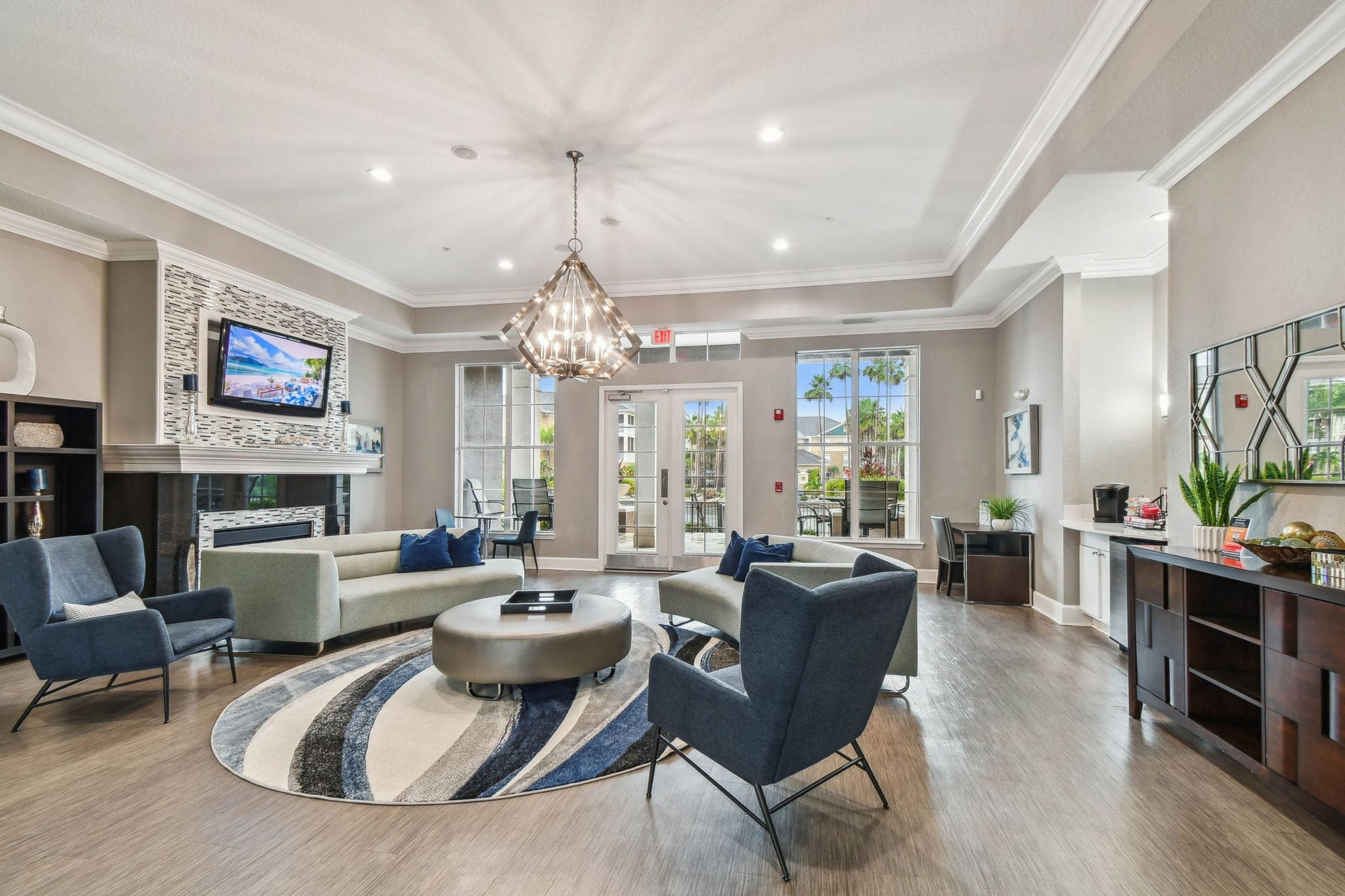 Alternate view of the spacious clubhouse showing natural light from tall windows, multiple seating areas, and access to an outdoor patio.