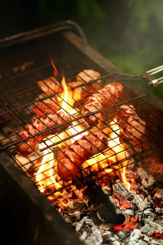 Delicious grilled sausages roasting on grates with flames and smoke