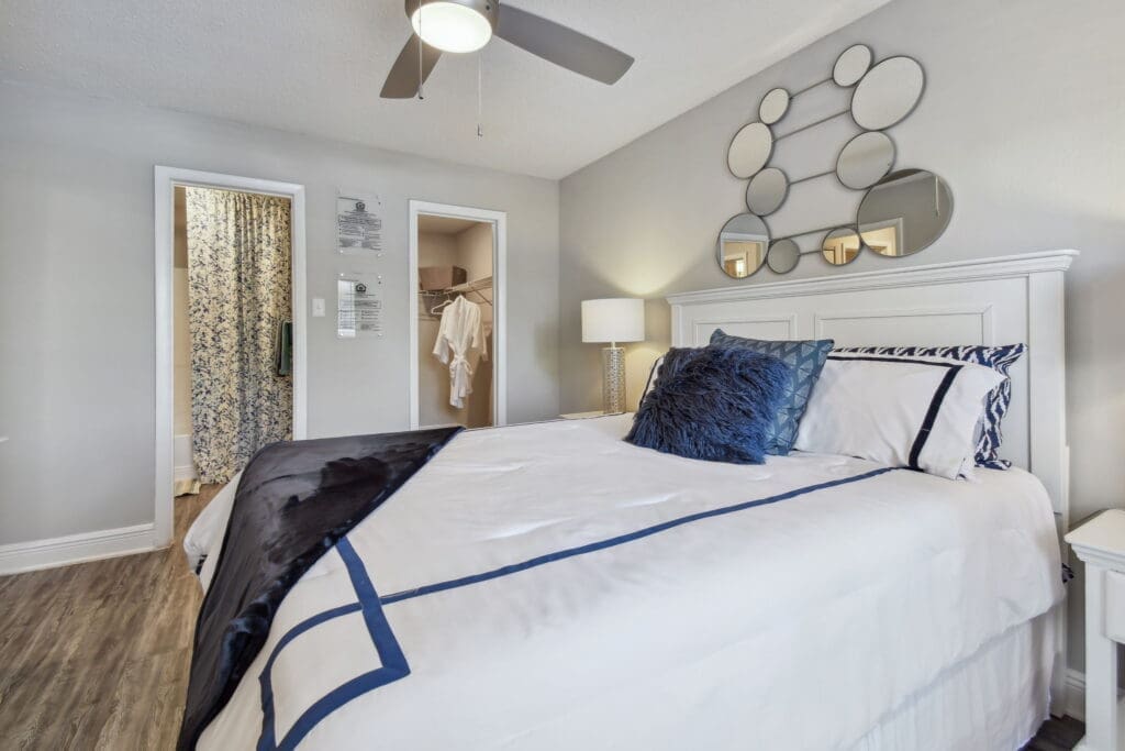 1-Bedroom Apartments in Largo, FL - Enclave on East - Bedroom with Wood-Inspired Flooring, Large Bed, Nightstand with Lamp, Ceiling Fan, Spacious Closet, and Attached Bathroom.