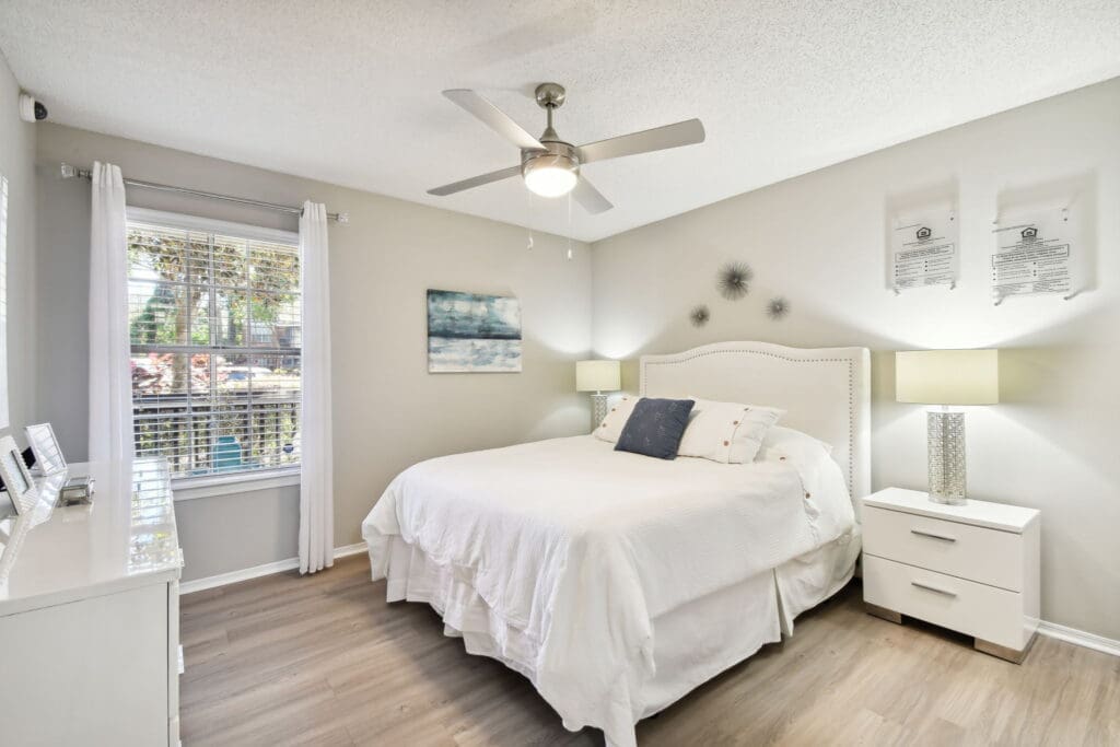 Lake Underhill, FL, Apartments Near Orlando Executive Airport - Enclave At Lake Underhill Apartments - Spacious Bedroom With Wood-Inspired Flooring, Large Bed, Nightstands With Lamps, Dresser, Ceiling Fan, And Large Window.