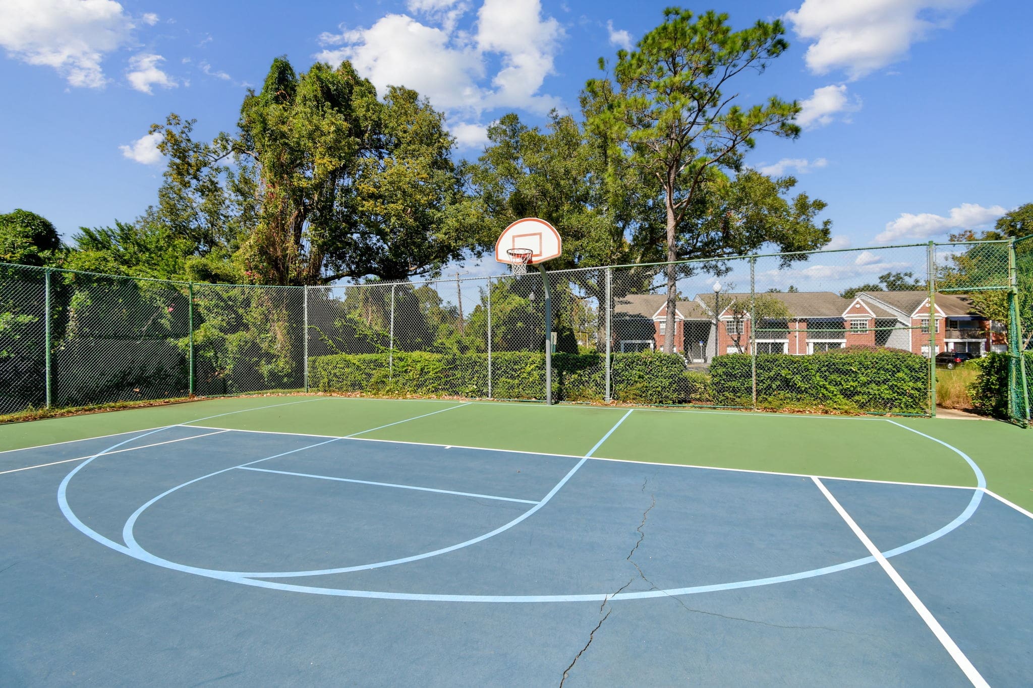 Lake Underhill, FL, Apartments Near Baldwin Park - Enclave At Lake Underhill Apartments - Fenced-In Basketball Court Surrounded By Manicured Hedgerows And Trees.