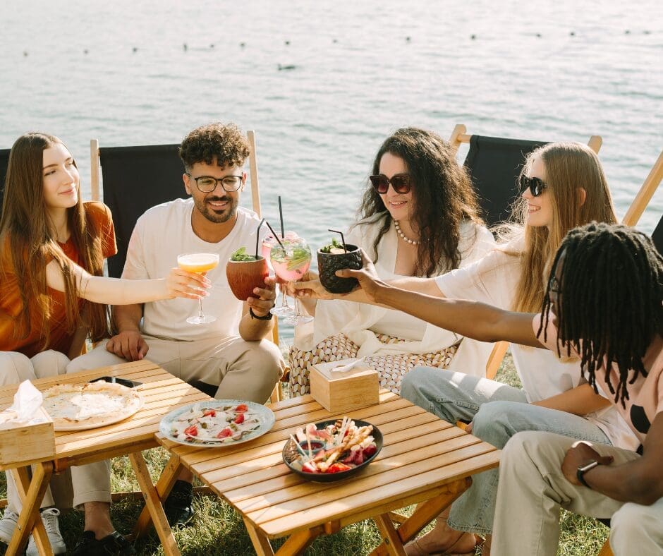 A group of friends sitting at an outdoor table by the waterfront with drinks in their hands